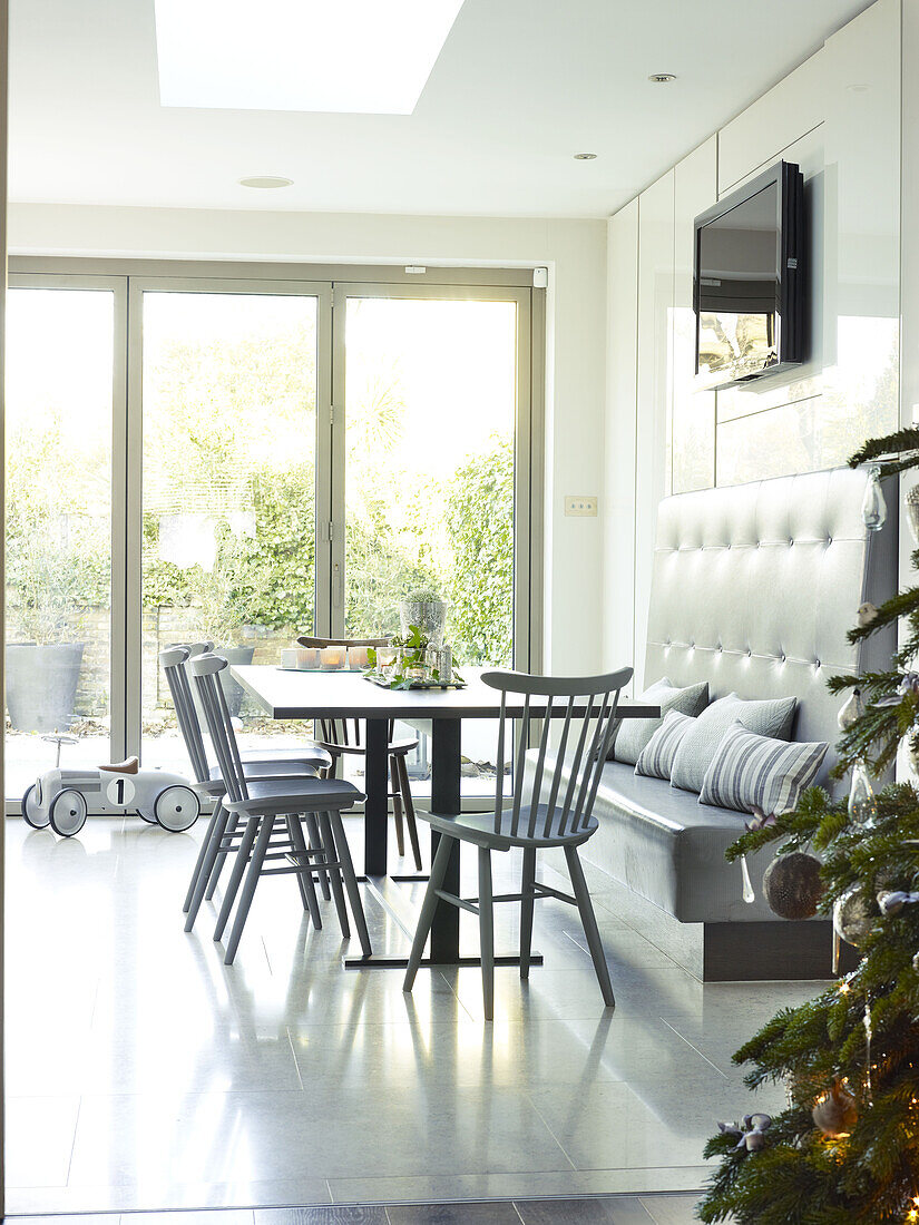 Grau gestrichene Stühle am Tisch mit Sitzbank und Terrassentüren in einem Haus in London, England, UK