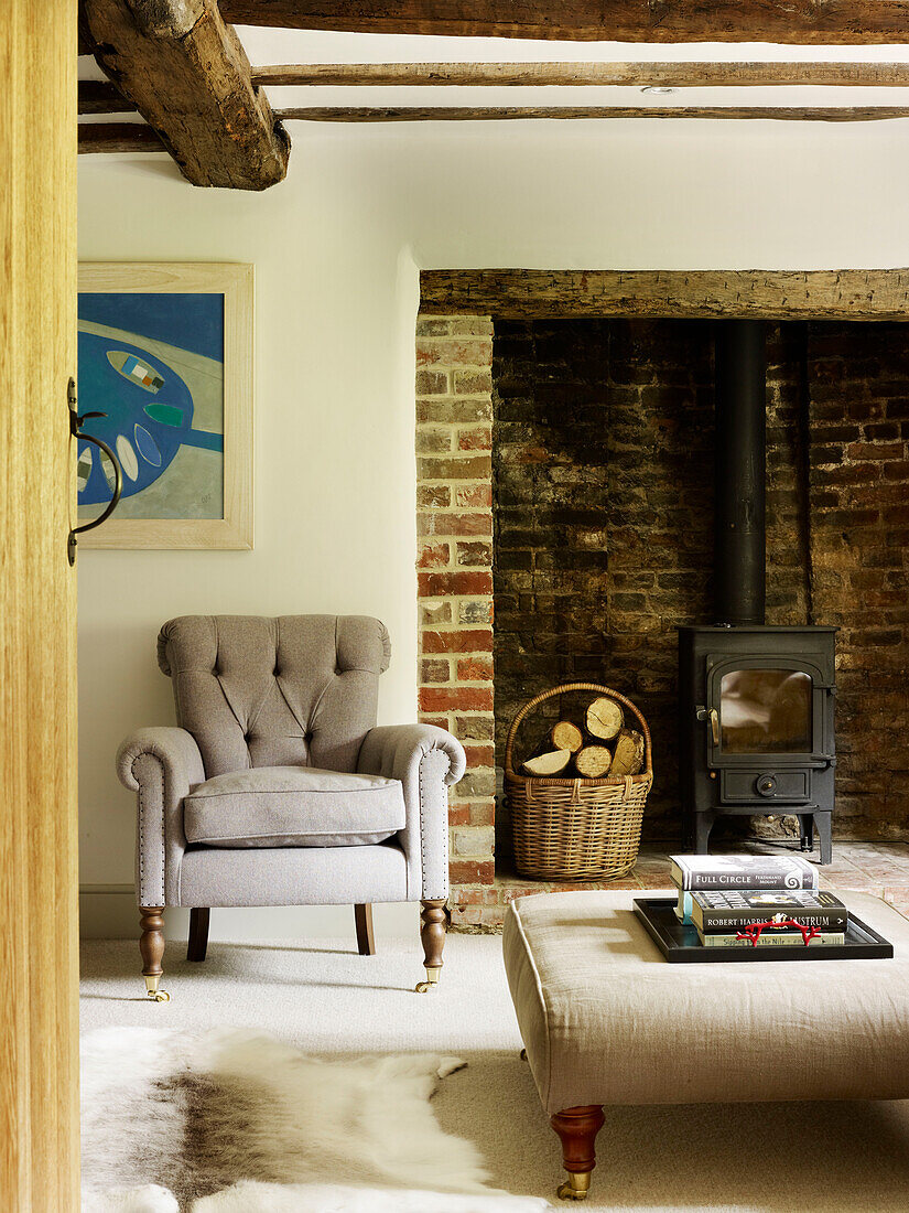 Sessel mit Knöpfen und Holzkorb am Kamin in einem Bauernhaus in West Sussex, England, Vereinigtes Königreich