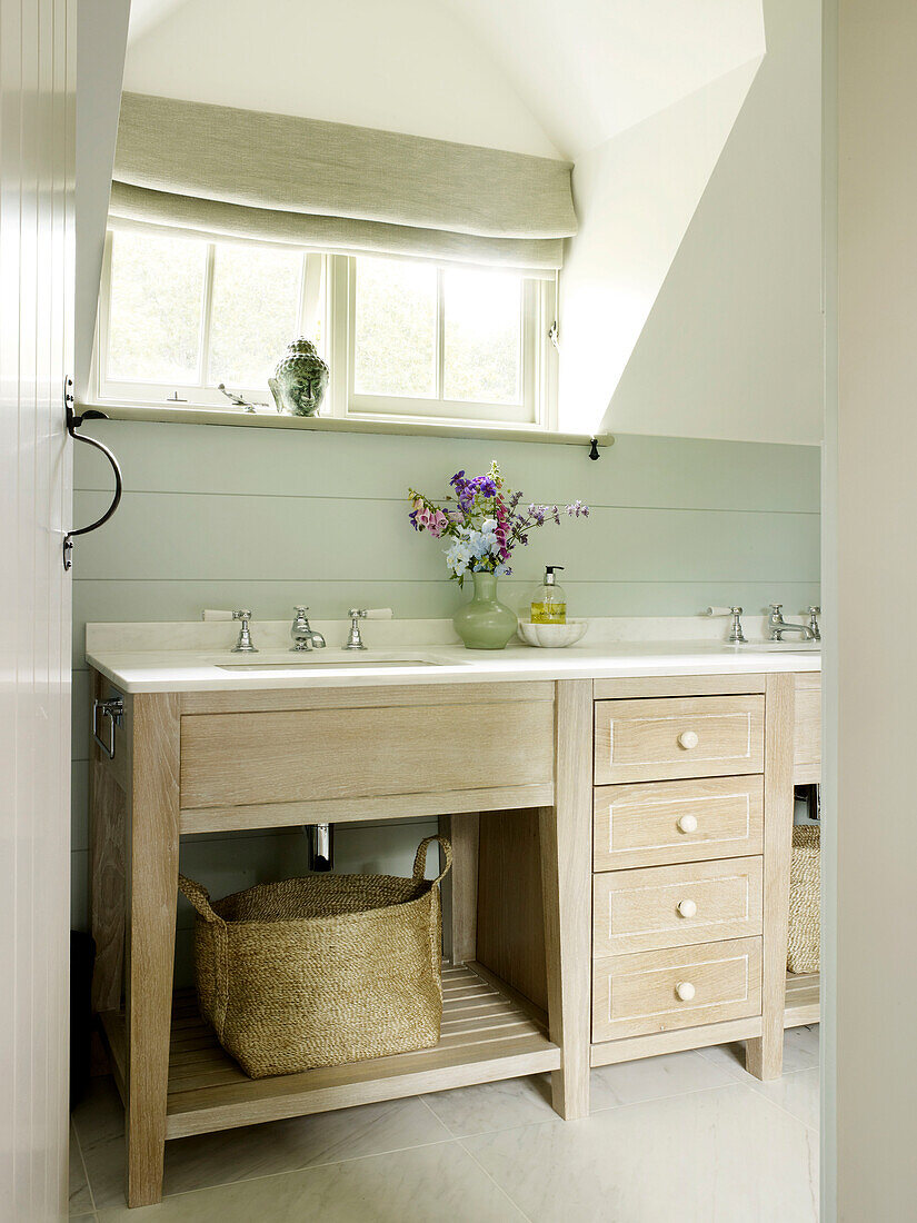 Cut flowers on pale wooden wash-stand below window in West Sussex farmhouse, England, UK