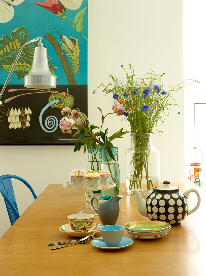 Teekanne und Schnittblumen auf Holztisch mit Kunstwerk in Londoner Familienhaushalt, UK