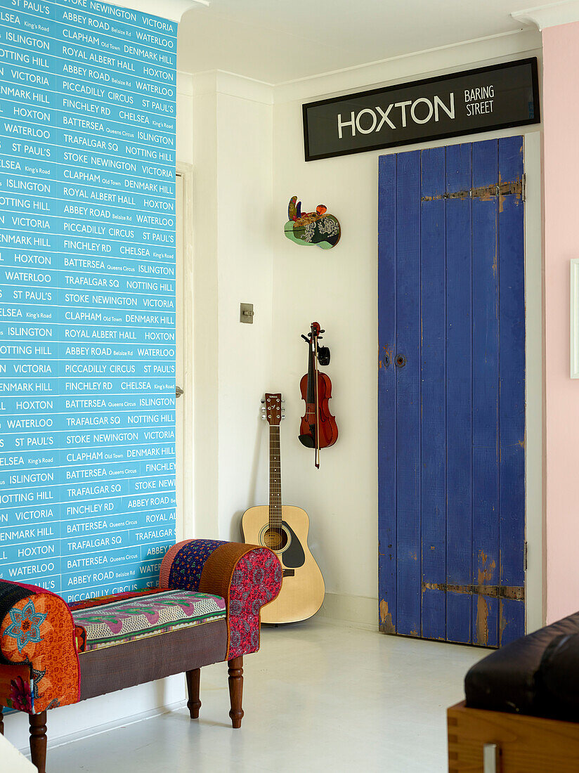 Upholstered bench seat with salvaged signs and stringed instruments in London family home, UK