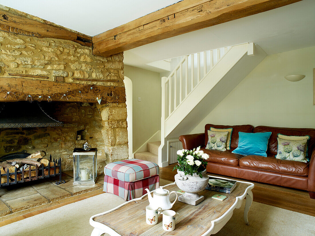 brown leather sofa with exposed stone fireplace in Oxfordshire cottage, England, UK
