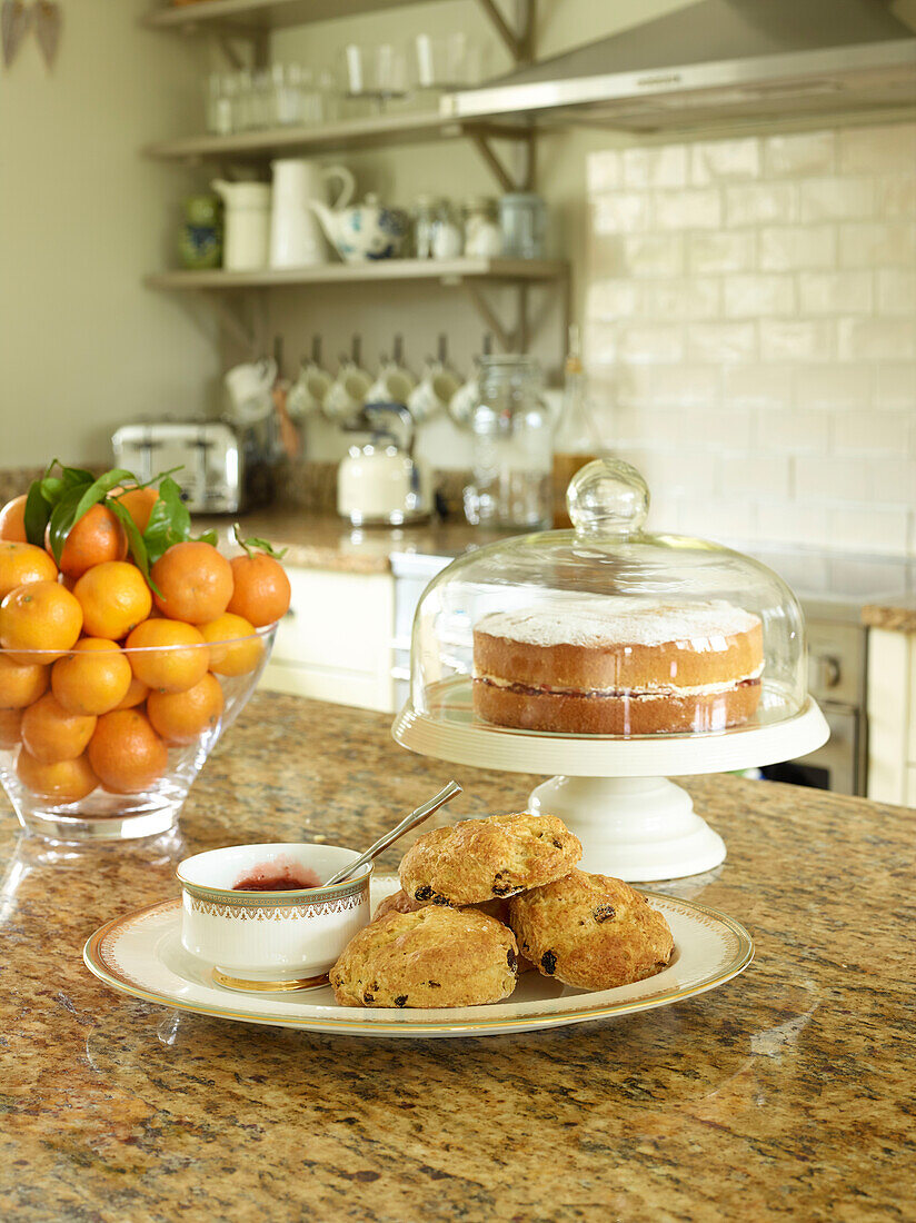 Sponge cake and tangerines with scones and jam on marble worktop in Oxfordshire cottage, England, UK