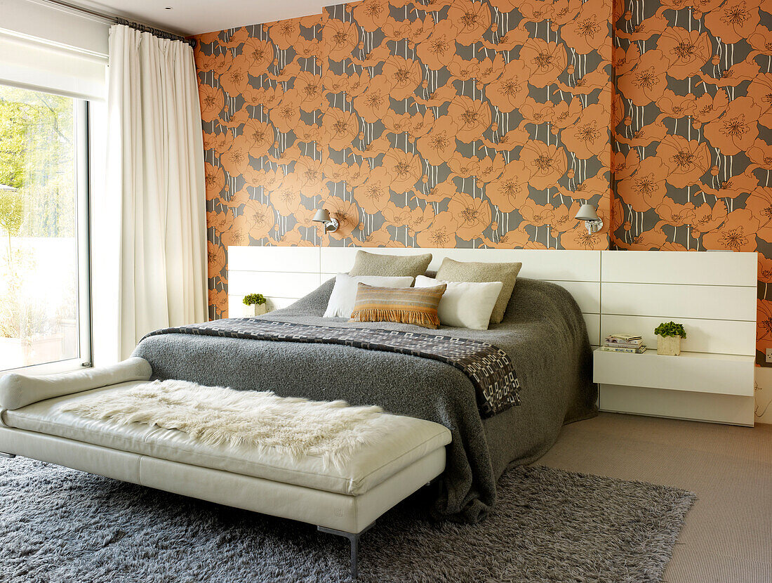 White leather lounger at foot of double bed with orange floral wallpaper in London home, UK