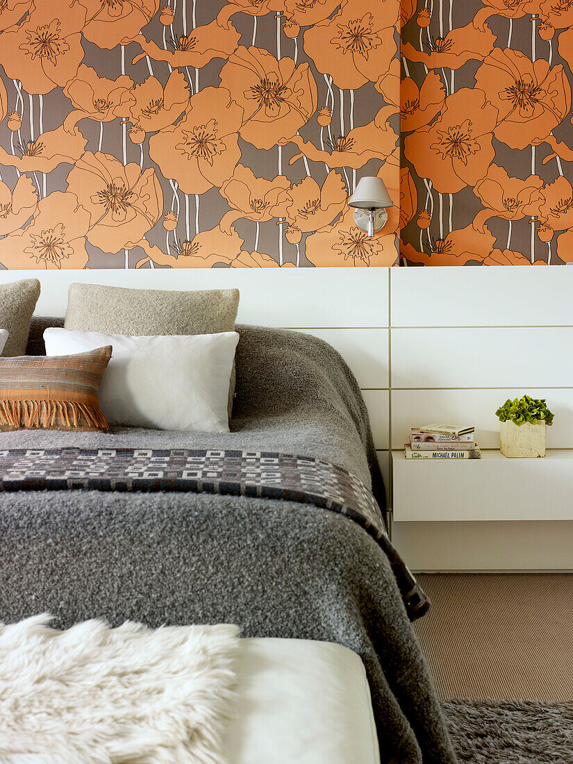Grey blankets on double bed with orange floral wallpaper in London home, UK