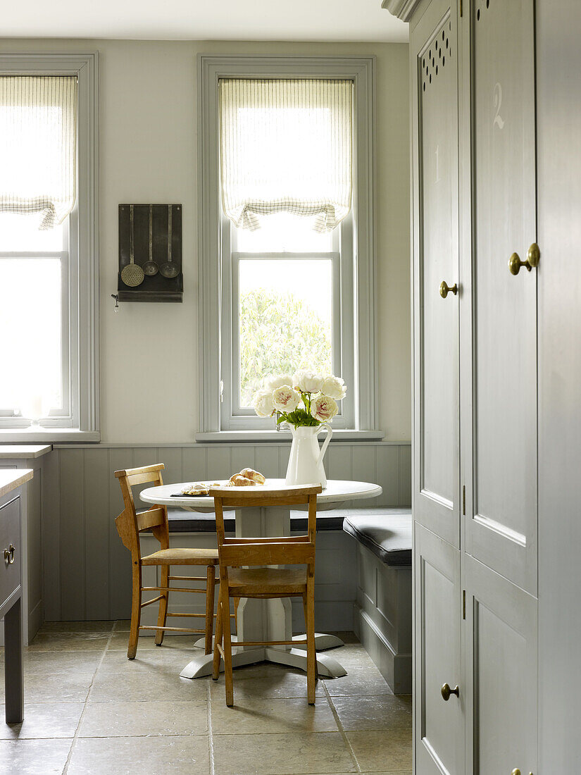 Kitchen table with pew chairs at window in grey painted kitchen East Sussex country house England UK
