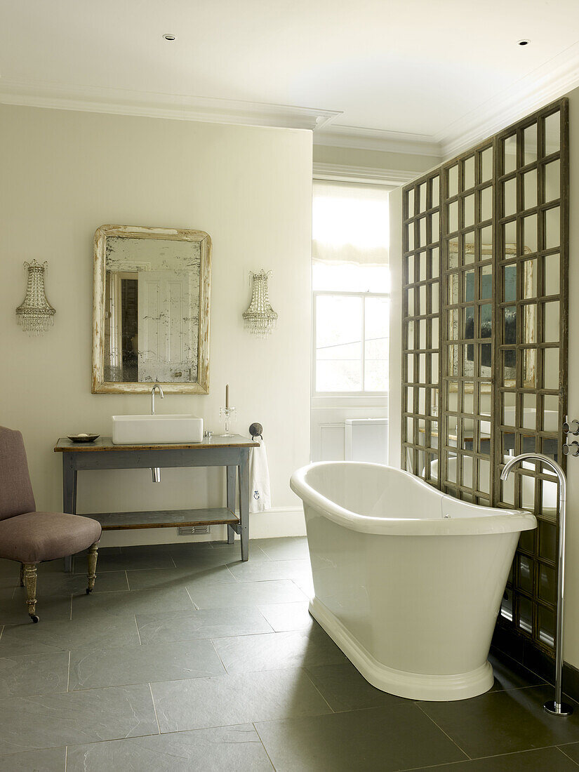 Freistehende Badewanne mit Silberspiegel-Waschtisch und verspiegeltem Wanddetail in einem Landhaus in East Sussex, England, UK
