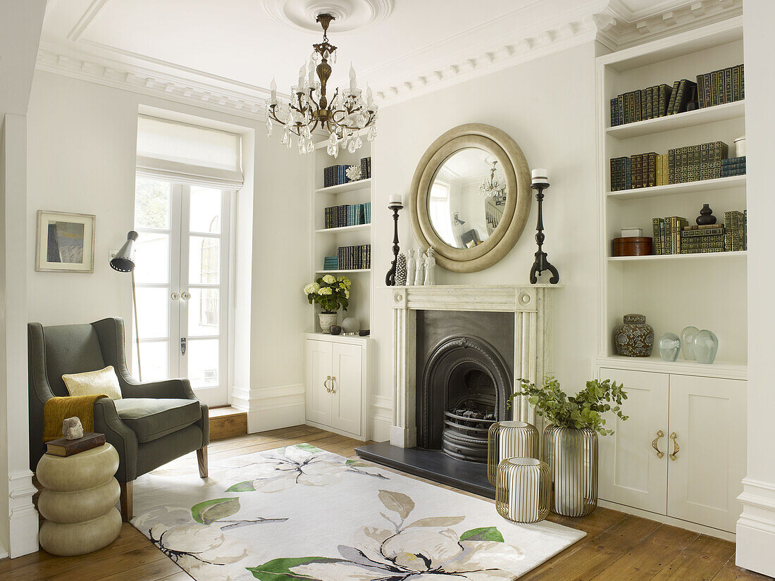 Circular mirror above fireplace with bookshelves in living room with grey armchair North London townhouse England UK
