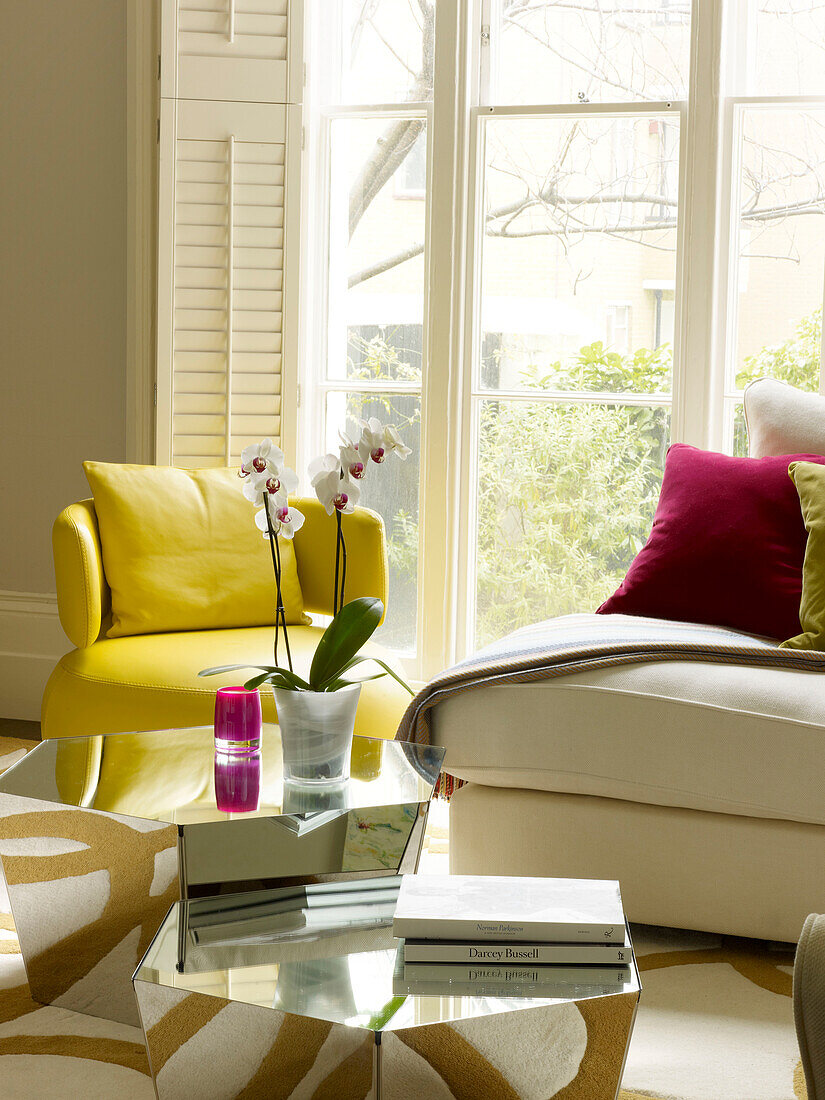 Orchid and books on mirrored coffee table with yellow leather armchair in living room in Little Venice townhouse London England UK