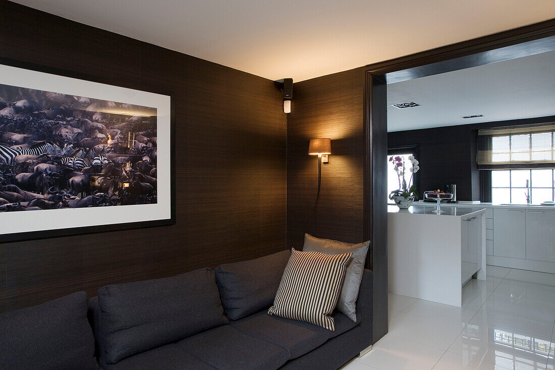 Grey sofa and artwork with view through doorway to modern kitchen in London home UK