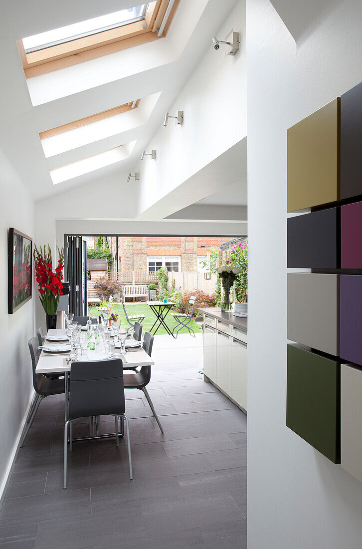 Esstisch unter Oberlichtern mit Kunstwerken in offener Küchenerweiterung eines modernen Hauses in London, England, UK