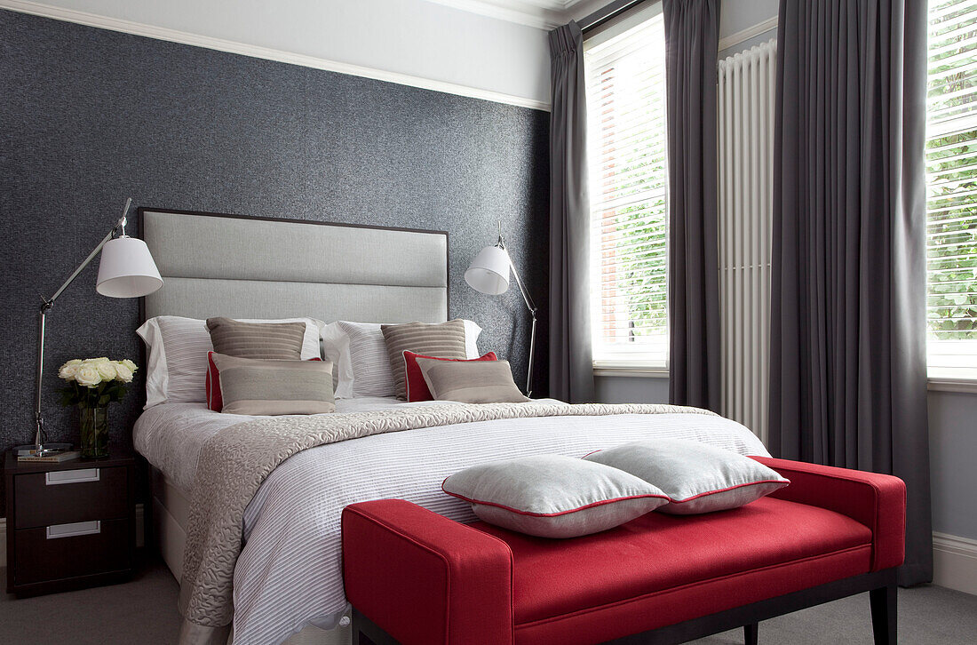 Muted grey bedroom with red footstool and matching anglepoise bedside lamps in contemporary London home, England, UK
