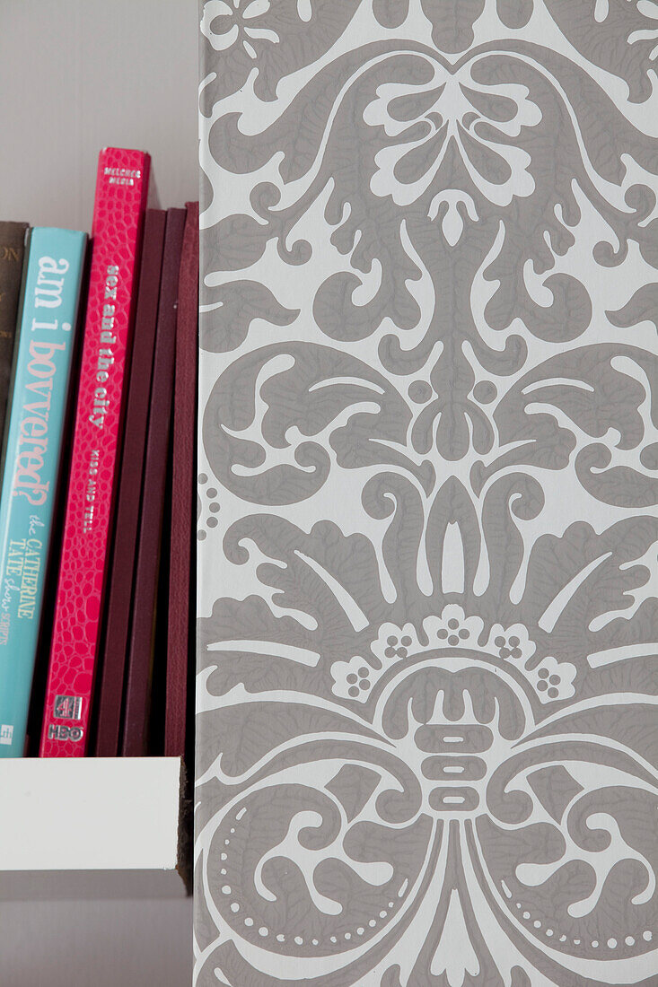 Bücher auf einem Regal mit grau gemusterter Tapete in einem modernen Haus in London, England, UK