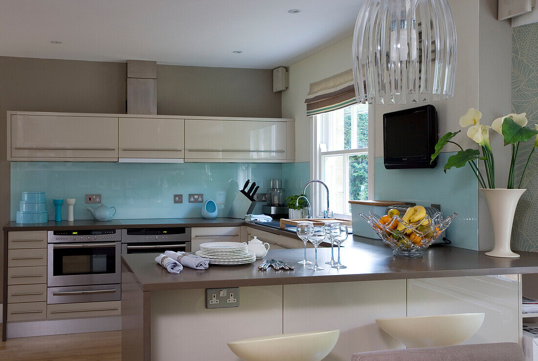 Glas-Pendelleuchte in einer Küche in Cambridgeshire mit hellblauer Spritzwand und weißen Einbaumöbeln UK