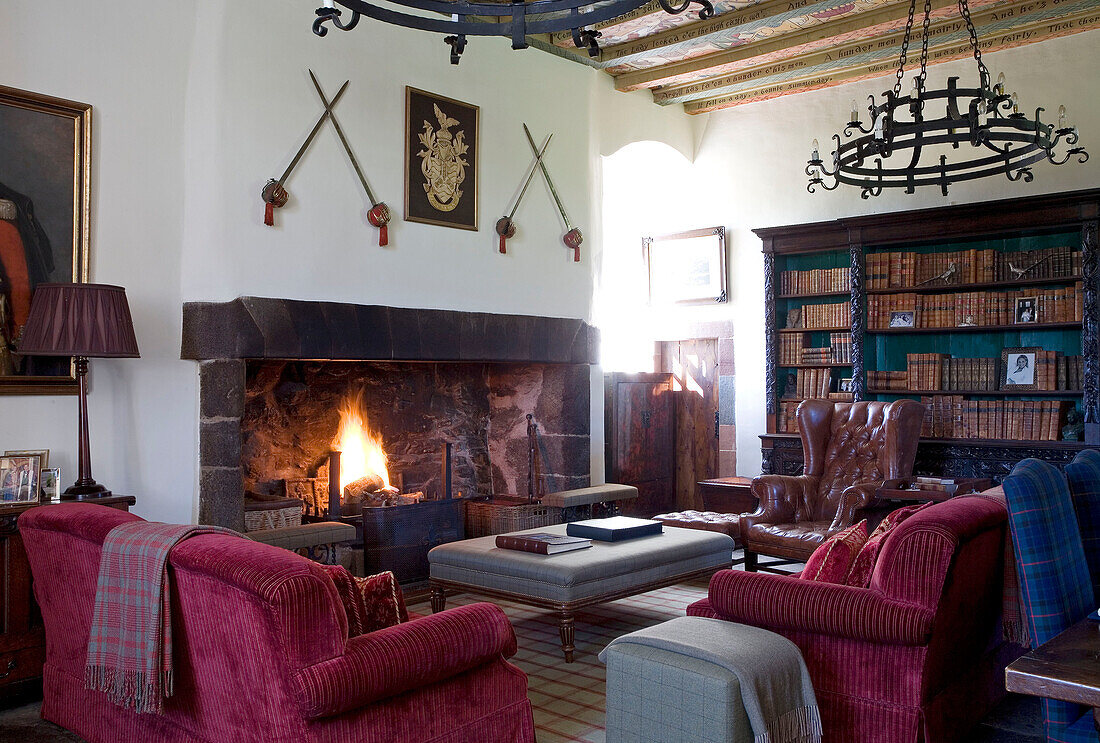 Pink sofas at lit fire with bookcase and swords Scotland UK