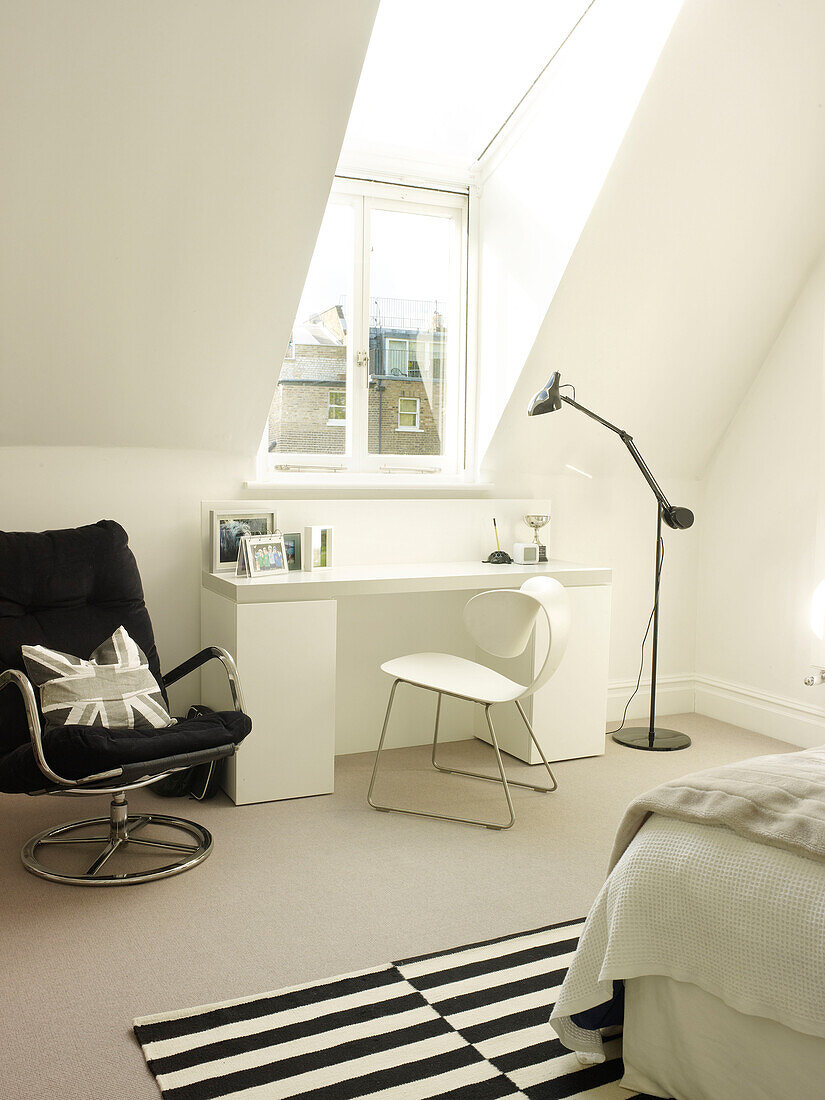 Schreibtisch und Stühle mit Lampe unter einer Dachgaube in einem Londoner Schlafzimmer, UK
