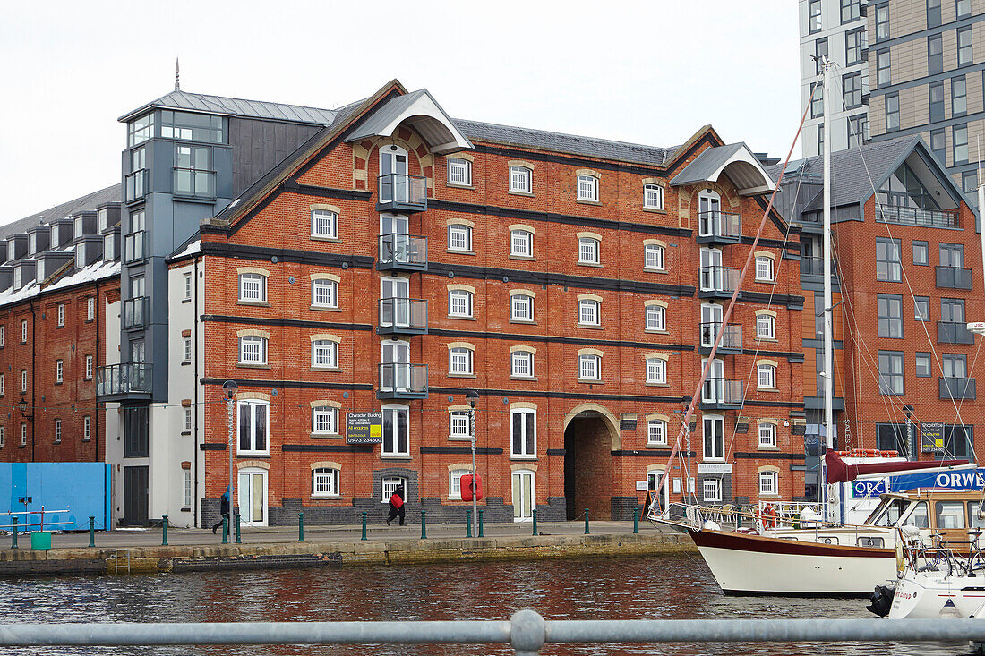 Brick warehouse conversion with yacht moored in Ipswich harbour, Suffolk, England, UK