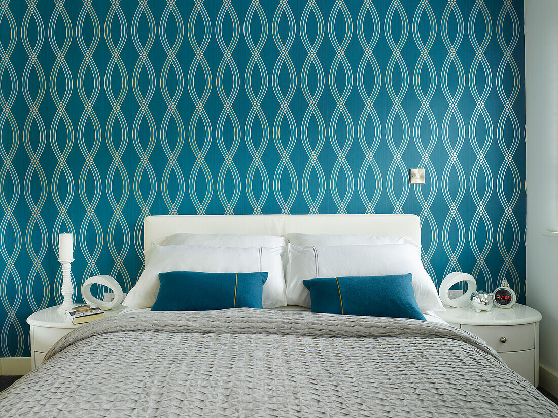 Blau gemusterte Tapete über einem Doppelbett mit weißen Beistelltischen in einer Wohnung in Manchester, England, UK