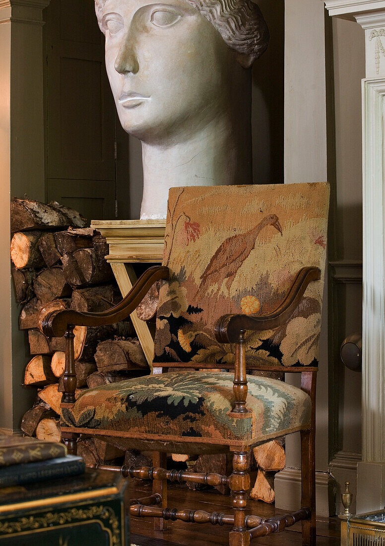 Gobelin-Sessel und geschnitzter Kopf mit Brennholz in einem Haus in Epsom Surrey UK