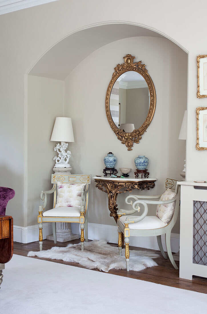Matching chairs with gilt oval mirror in alcove recess of historic country house