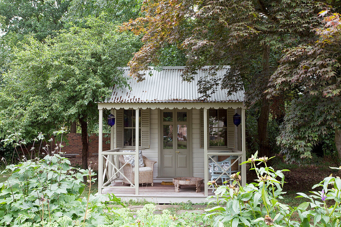 Gartenhaus mit Sitzgelegenheiten und blauen Laternen unter Bäumen