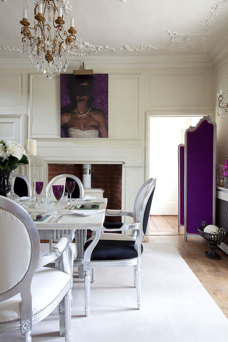 Black and white upholstered dining chairs at table below chandelier in dining room with purple folding screen
