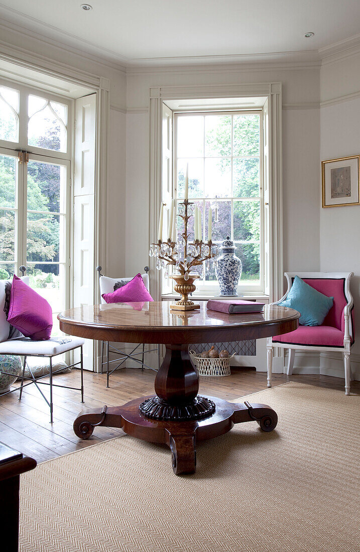 Round mahogany pedestal table with bright pink chair and cushions in Georgian style room