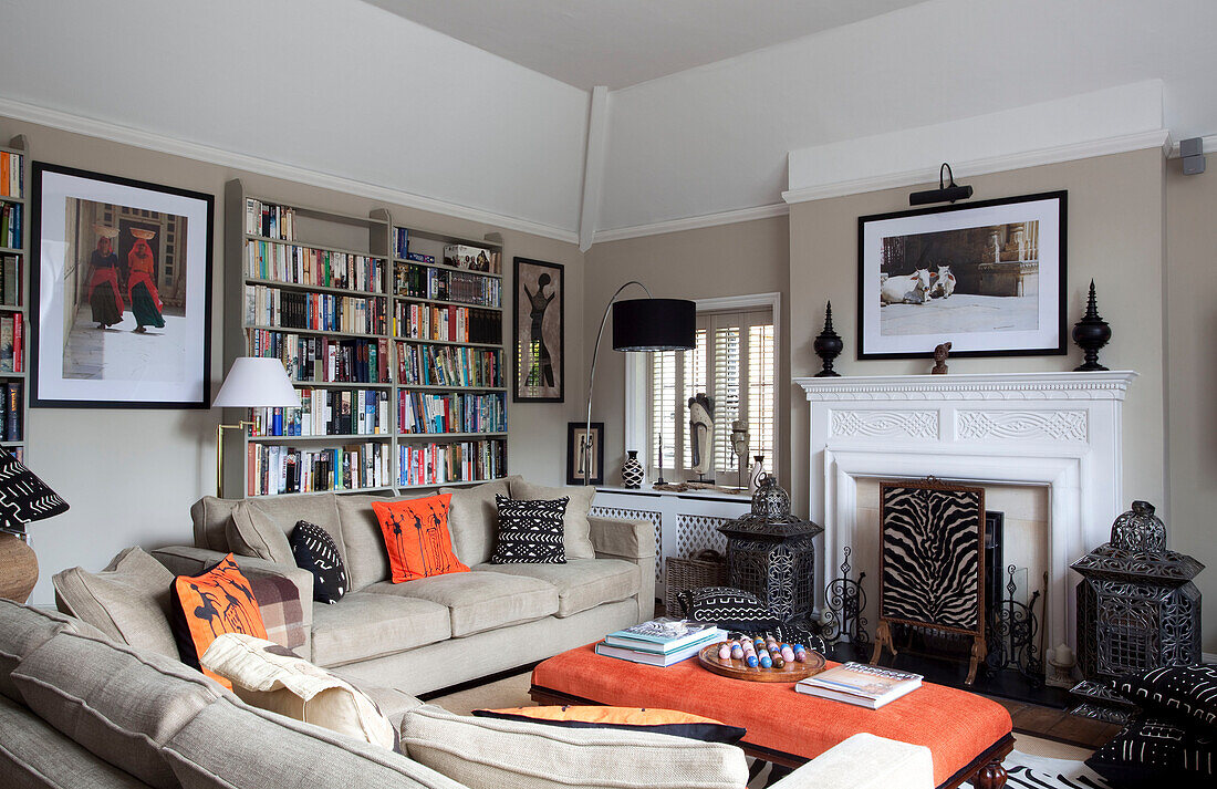 Wohnzimmer mit beigen Sofas und orangefarbenem Ottoman und einer Sammlung eklektischer Reiseerinnerungen