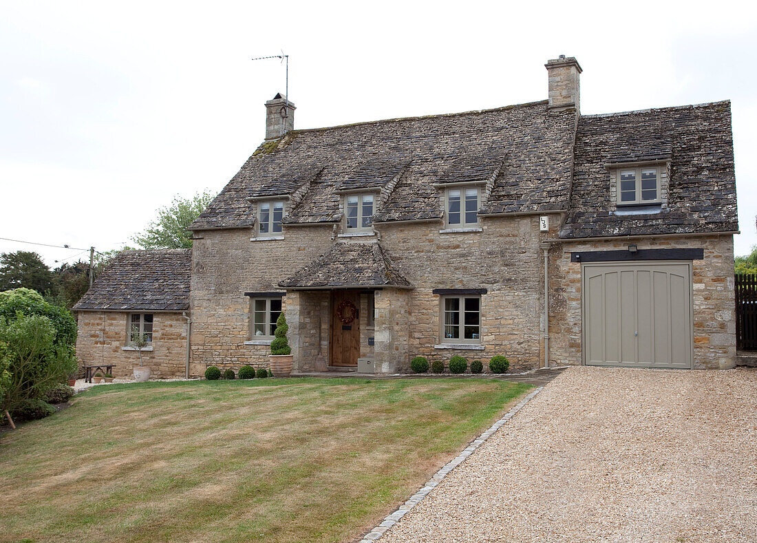 Gravel driveway and lawn at exterior of stone Cotswolds country house UK