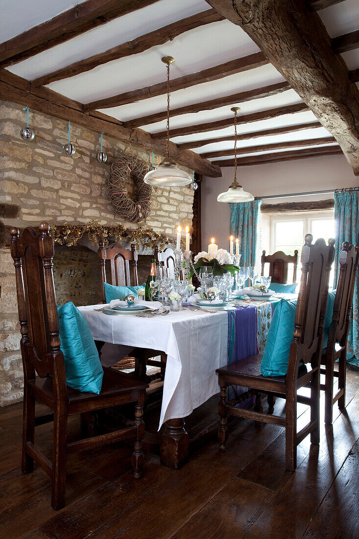 Turquoise cushions on dining chairs below beamed ceiling in Cotswolds home UK
