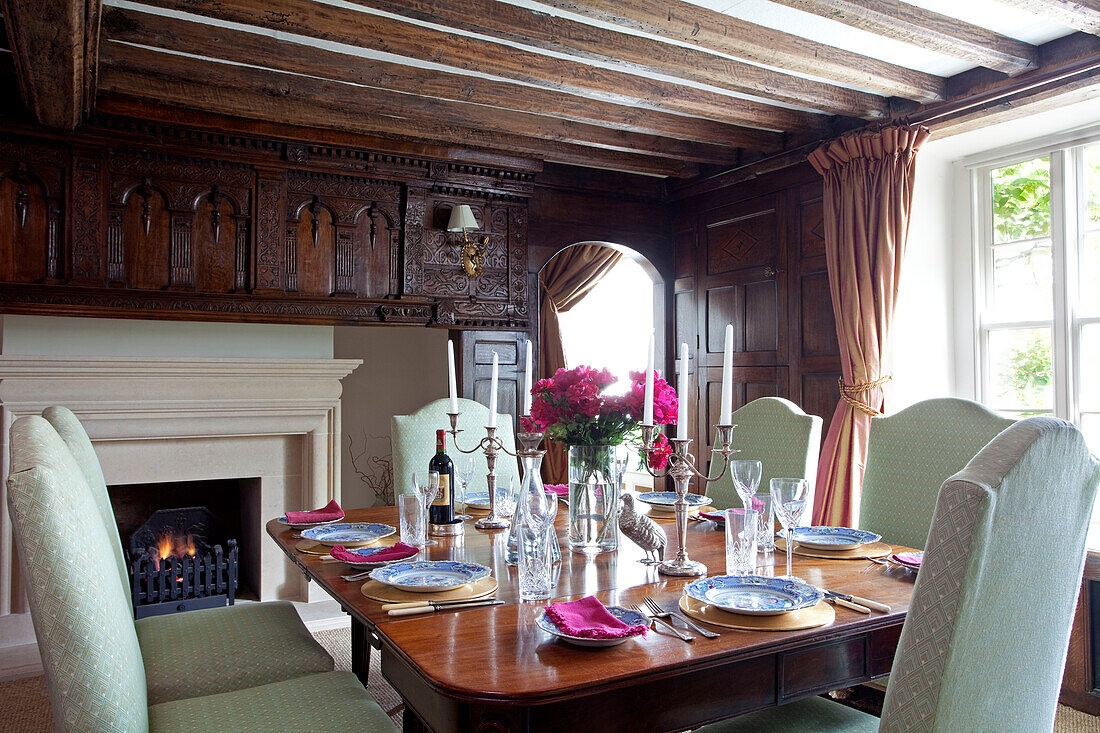 Lit fire in dining room with carved detailing and polished wooden table in East Sussex home, England, UK