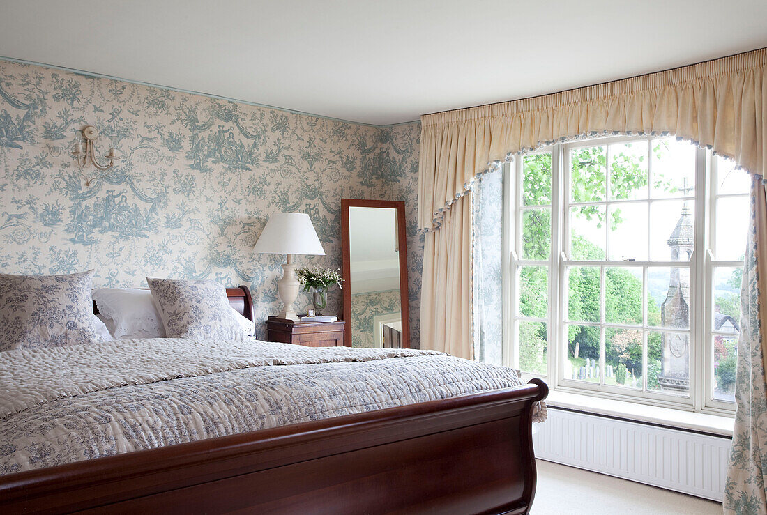 Polished wooden bed in room with toile wallpaper in East Sussex home, England, UK