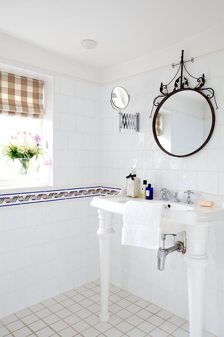 Runder Spiegel über dem Waschbecken in einem weiß gefliesten Badezimmer in einem Haus in East Sussex, England, Vereinigtes Königreich