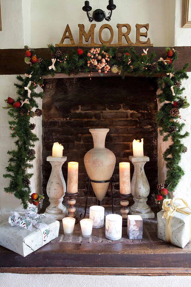 Lit candle and gifts in brick fireplace with Christmas garland Sussex UK