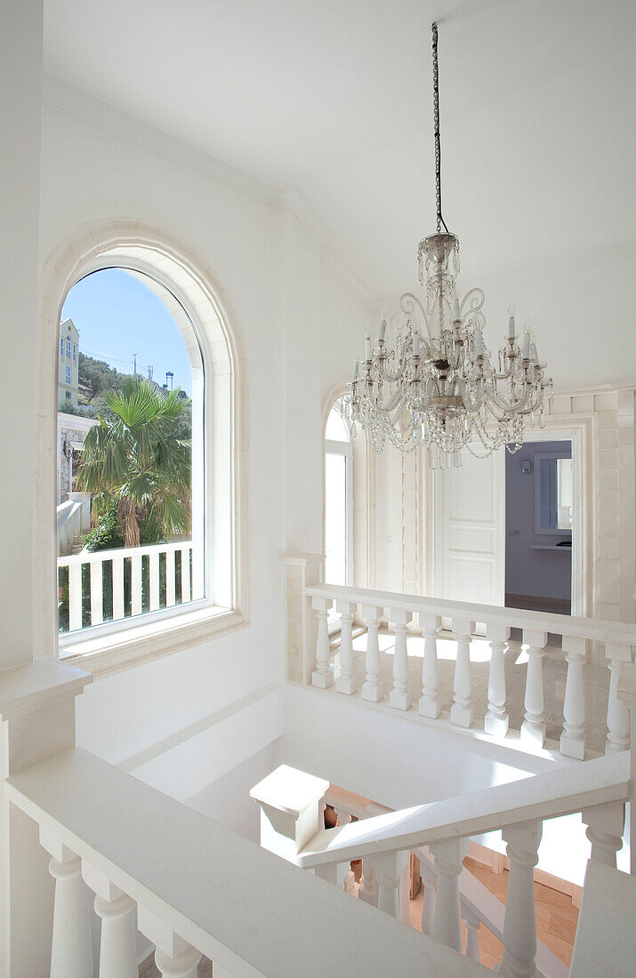 Glass chandelier hangs above white staircase with arched window in holiday villa, Republic of Turkey