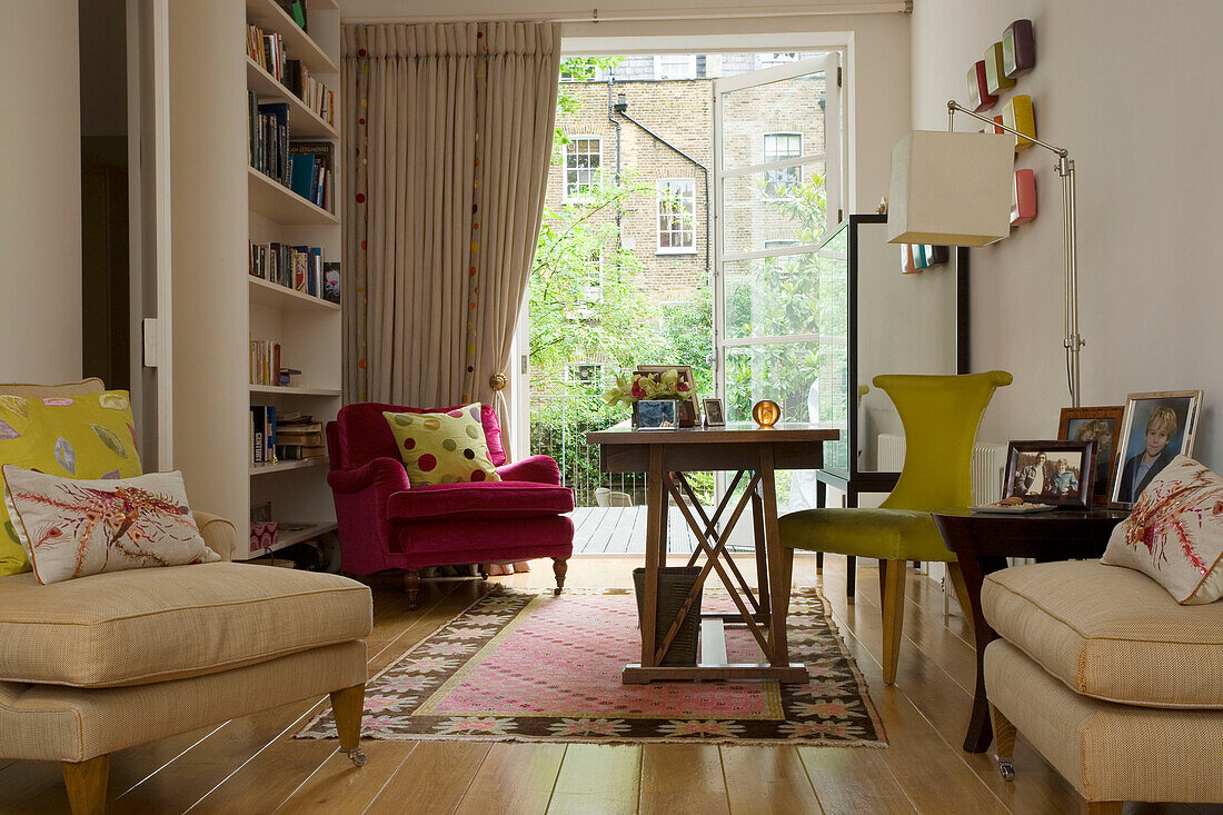 Armchairs with bright cushions and bookshelf in London home UK