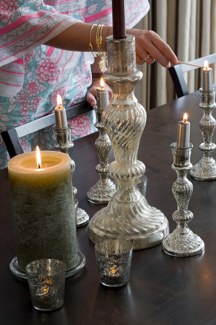 Woman lighting silver candlesticks on dining table London UK