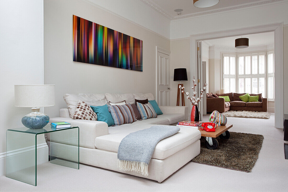 Coffee table with caster wheels and white sofa below modern art in double room of contemporary London home, UK