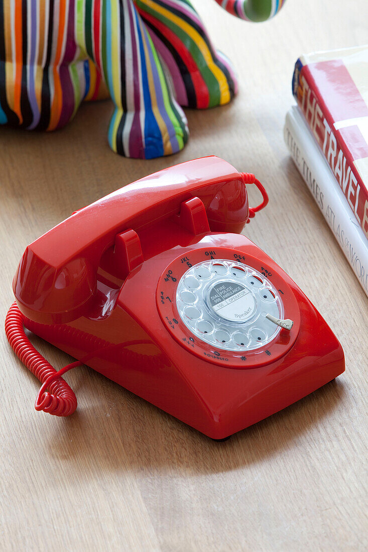 Red plastic rotary dial telephone on coffee table in contemporary London home, UK