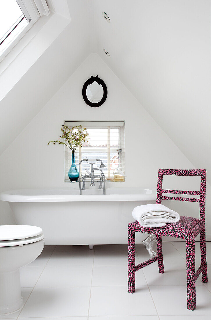 Freestanding bath and pink floral patterned chair in bathroom attic conversion in contemporary London home, UK
