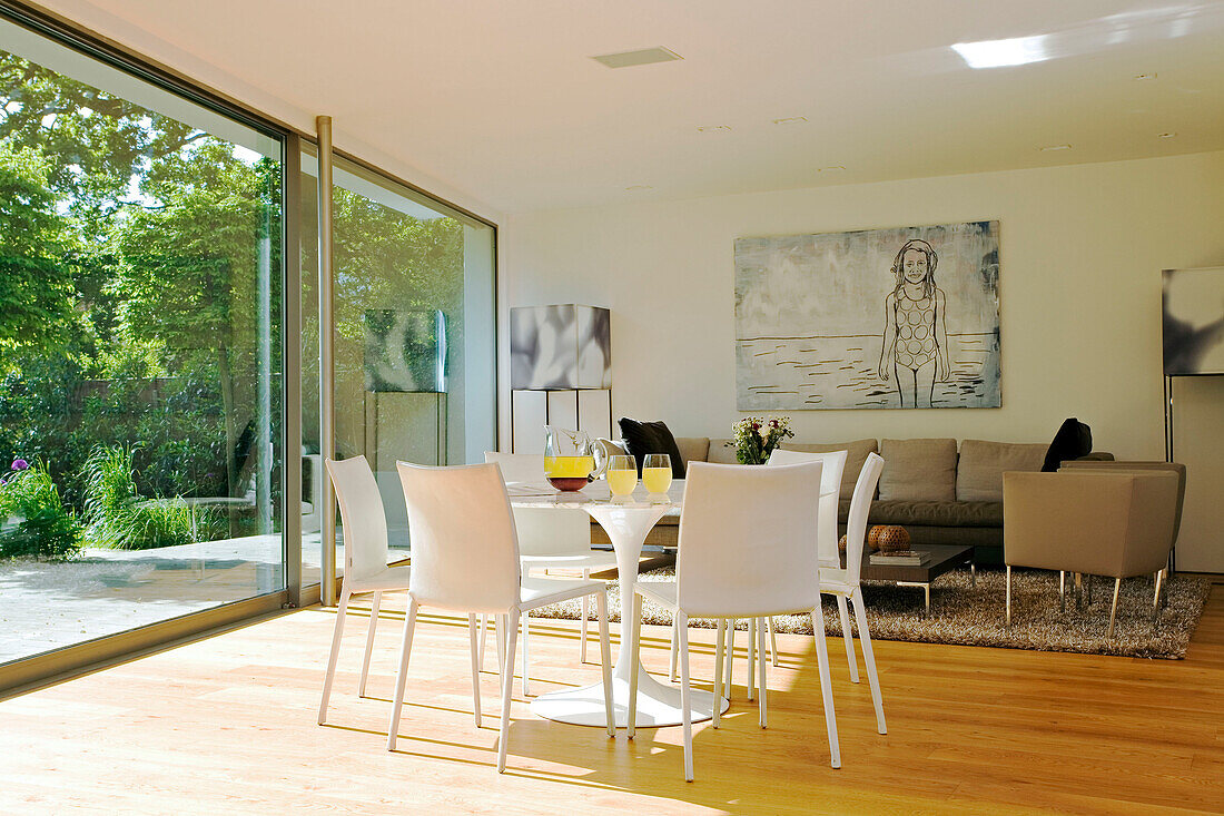 Tisch für sechs Personen im offenen Wohnbereich mit durchgehendem Fenster und Blick auf den Garten in einem modernen Londoner Haus, England, UK