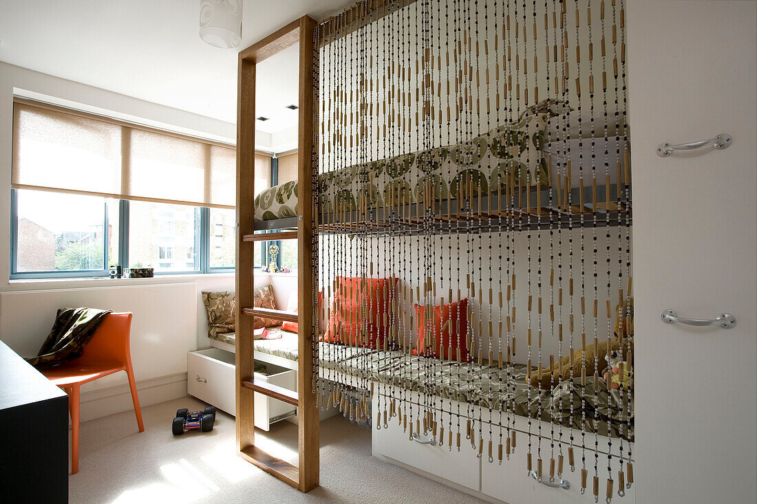 Childs room with beaded curtain over raised platform bed in London family home, England, UK
