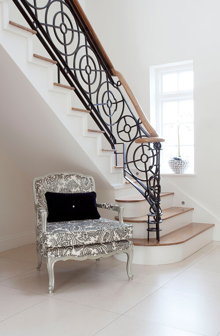 Black and white armchair under wrought iron staircase in Hendon home London UK