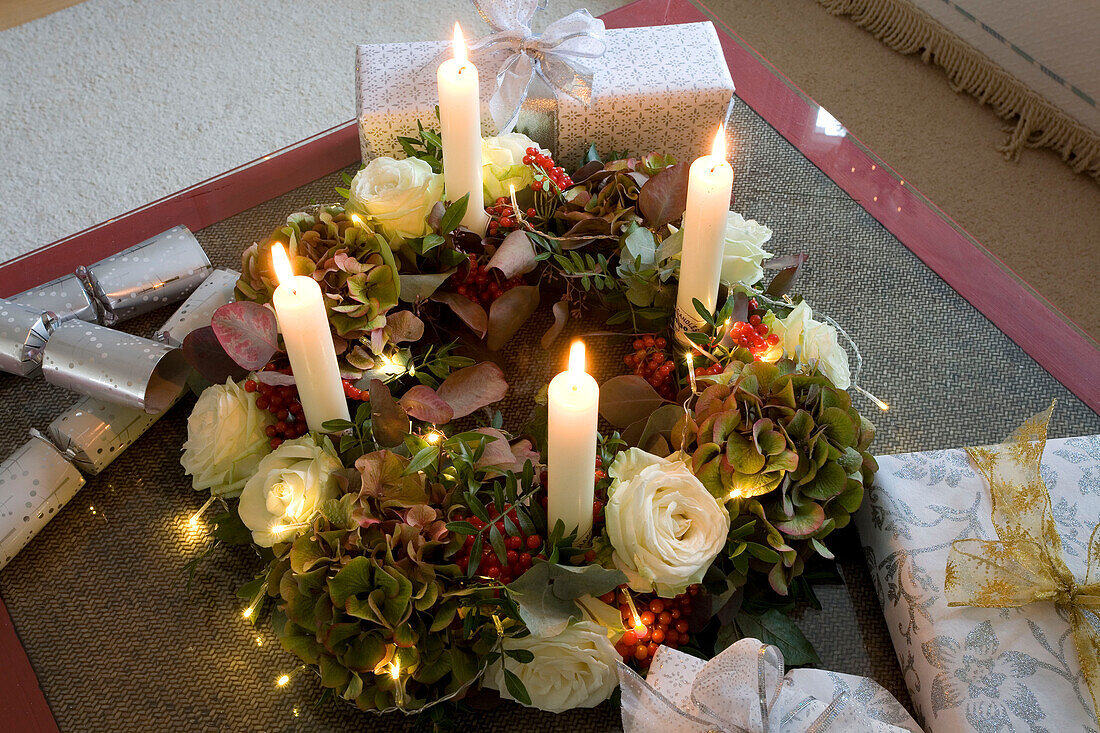 Lit candles and floral Christmas wreath on coffee table in living room of London home, UK