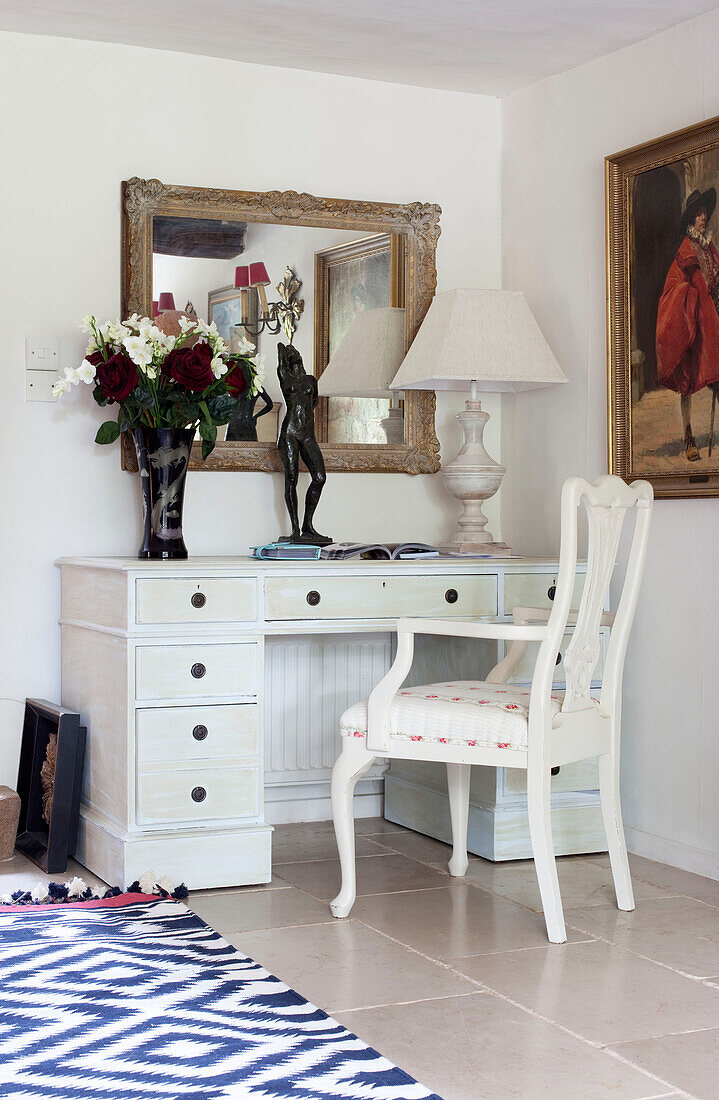 Cut flowers on painted desk with chair below mirror in hallway of Sussex farmhouse, UK