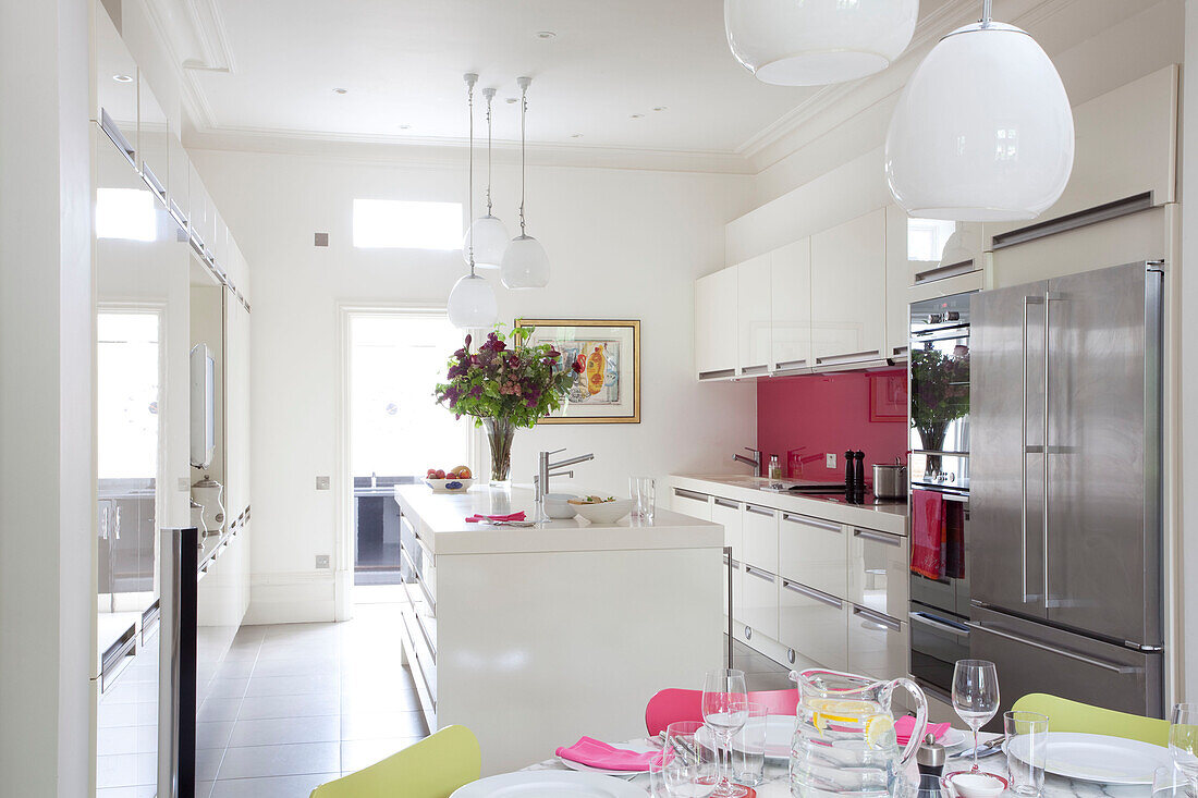 Cut flowers on island unit in kitchen with bright pink splashback, contemporary London home, UK