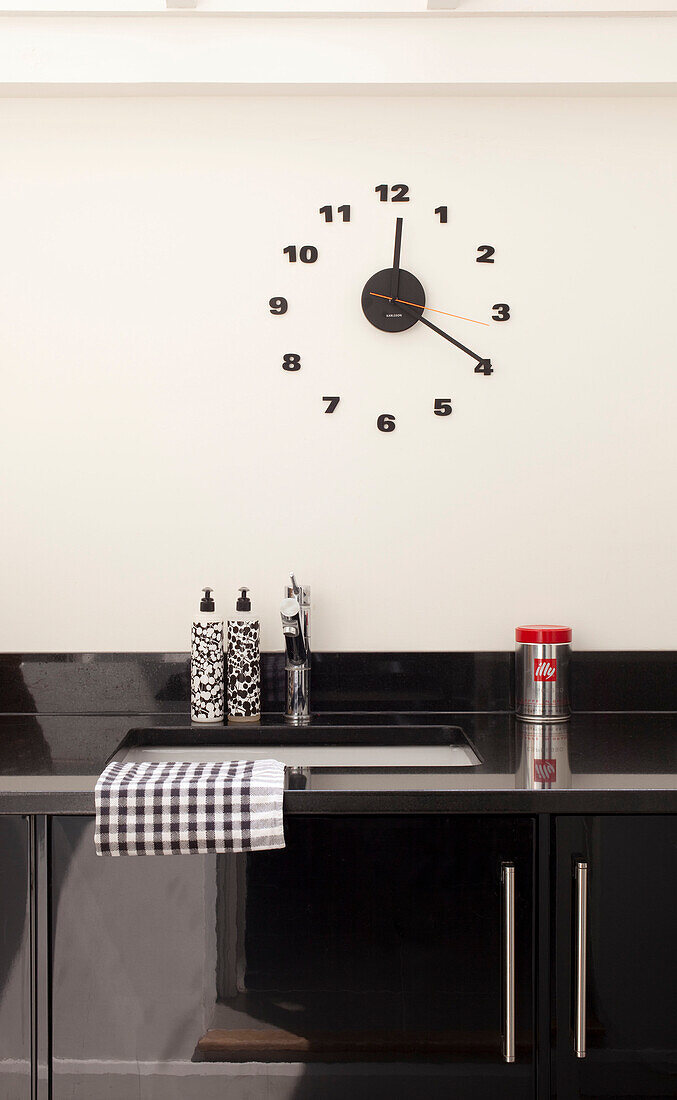 Wall mounted clock above black kitchen counter in contemporary London home, UK