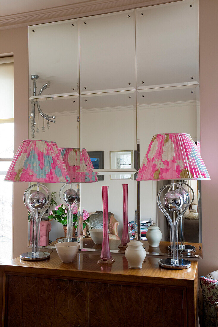 Matching lamps with pink shades on wooden sideboard mirrored in London home UK