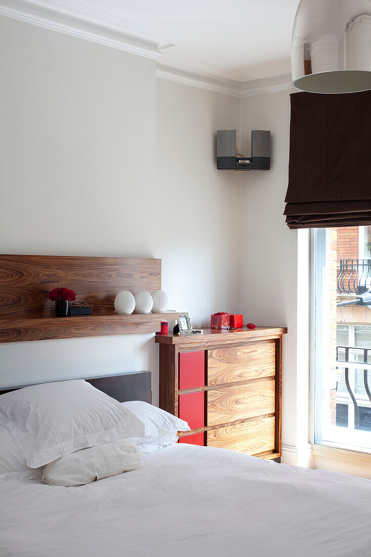 Holzkommode neben dem Bett mit weißen Kissen in einem Londoner Schlafzimmer UK