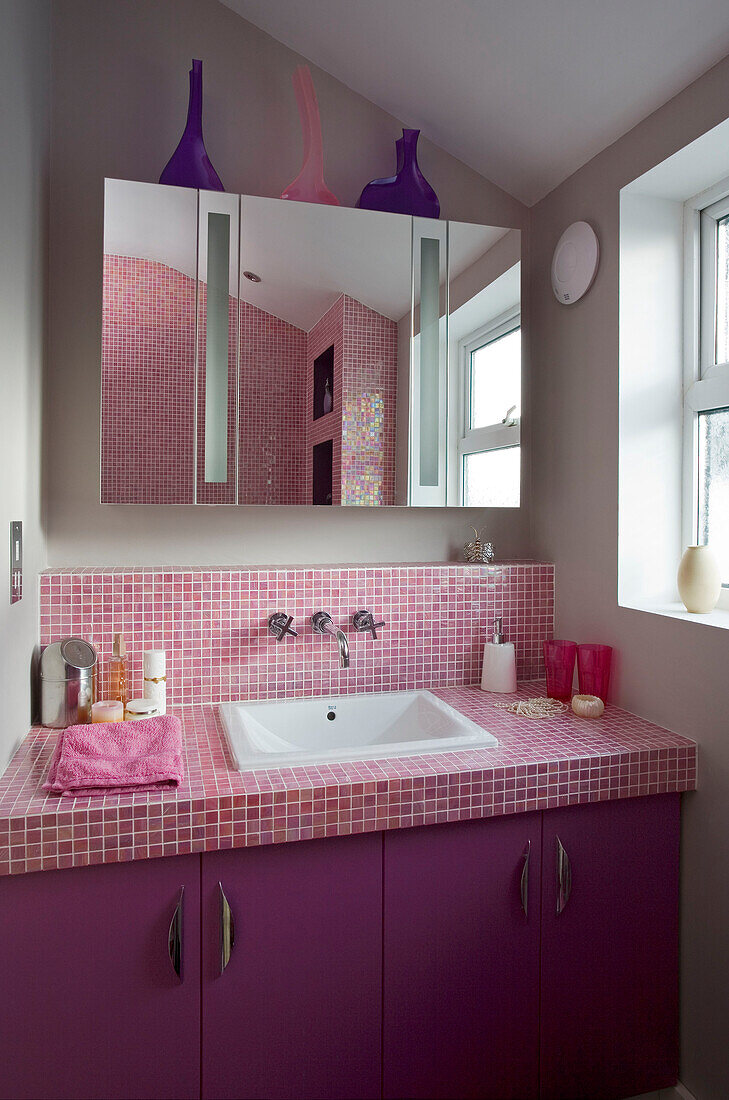 Spiegelschrank über rosa gefliestem Waschbecken in einem Haus im Retro-Stil in East Sussex, England, UK